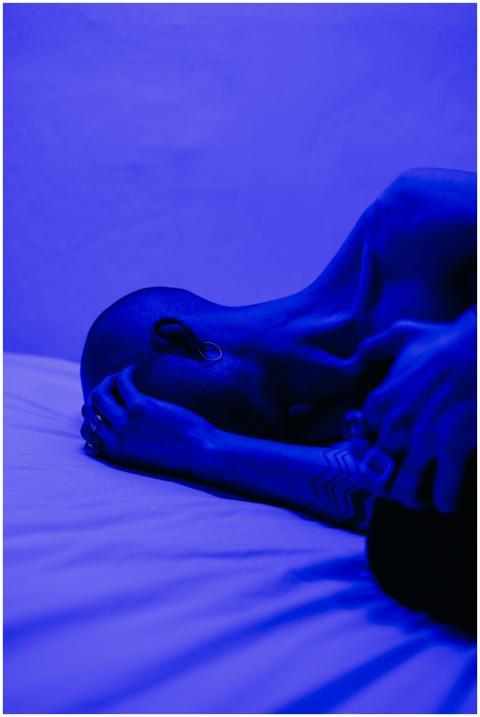 A tattooed man lying in blue light, symbolizing is