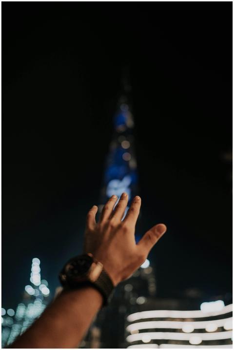 A hand reaches towards the illuminated Burj Khalif