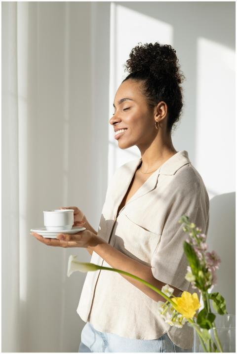 A woman stands smiling with a cup and saucer in na