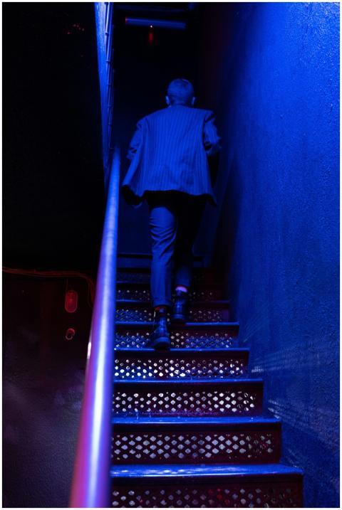 A man in a suit climbs dimly lit nightclub stairs