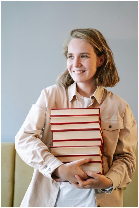 A young woman smiling while holding a stack of boo