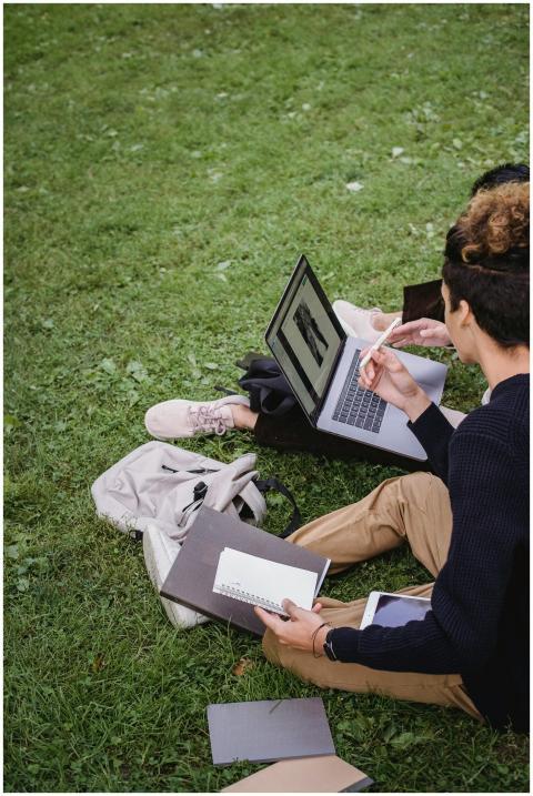 Two students study together on a laptop outdoors,