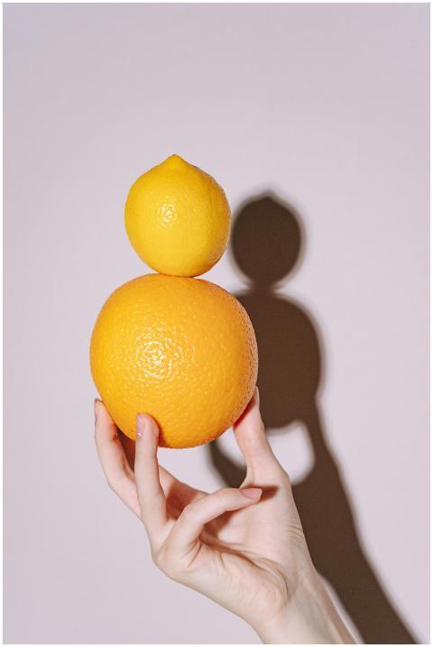 A hand balances an orange and a lemon, casting a c