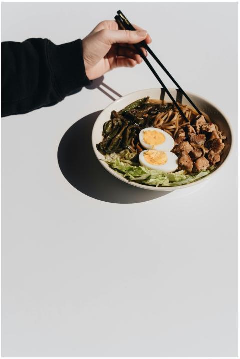 A person's hand reaches for a noodle bowl with cho
