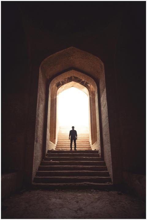 A solitary figure stands in a dramatic archway wit