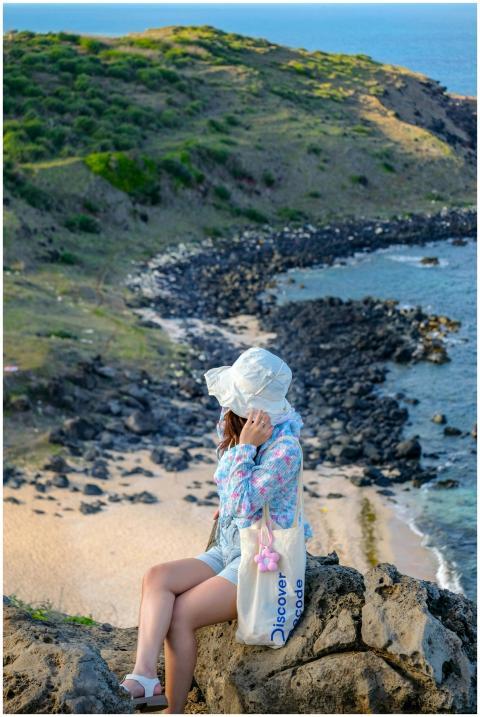 Woman in summer attire sitting on rocks overlookin