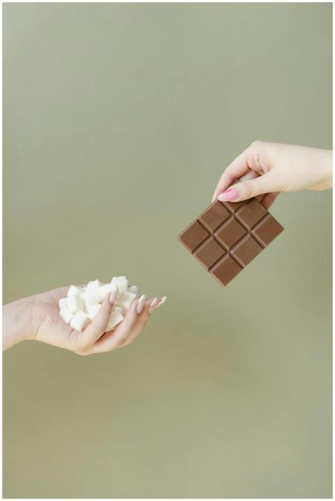 Two hands holding a chocolate bar and sugar cubes