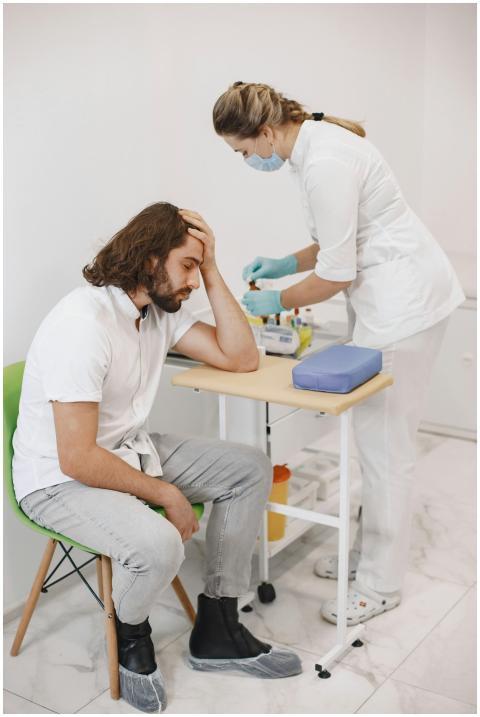 A nurse in medical gloves helps a seated patient i
