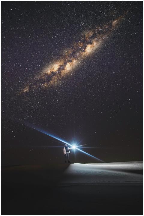 A lone person with a flashlight stands under a sta