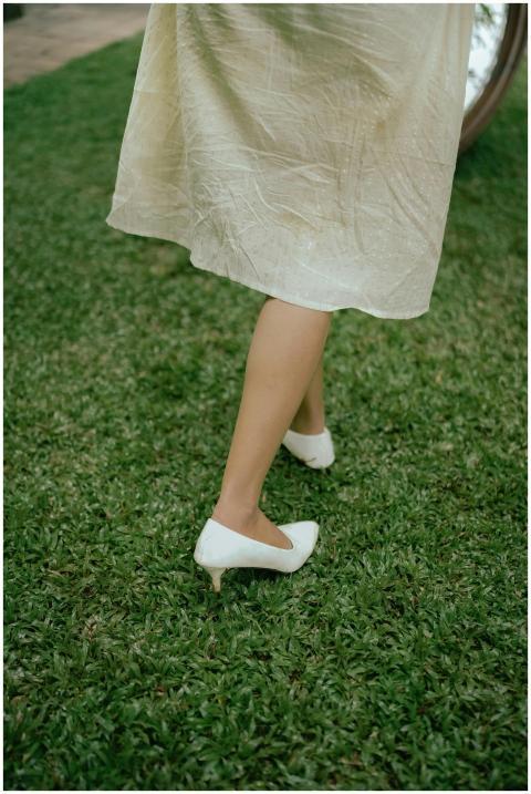 A woman in white heels walking on a lush green law