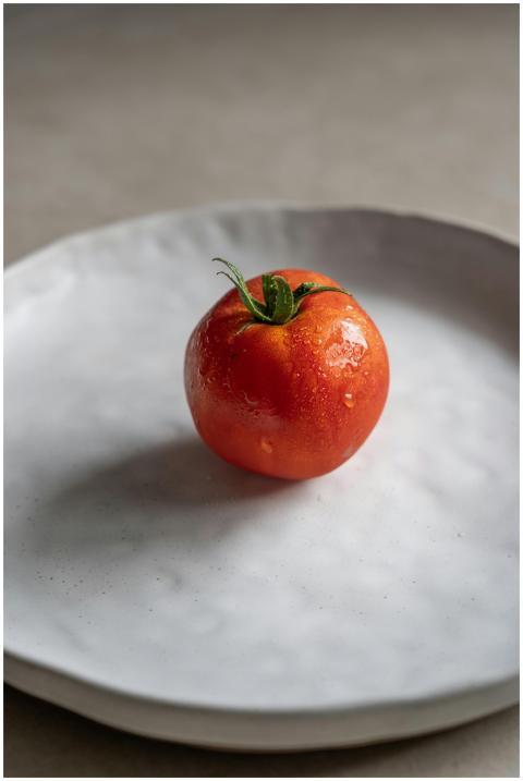 Juicy red tomato with water droplets on a white ce