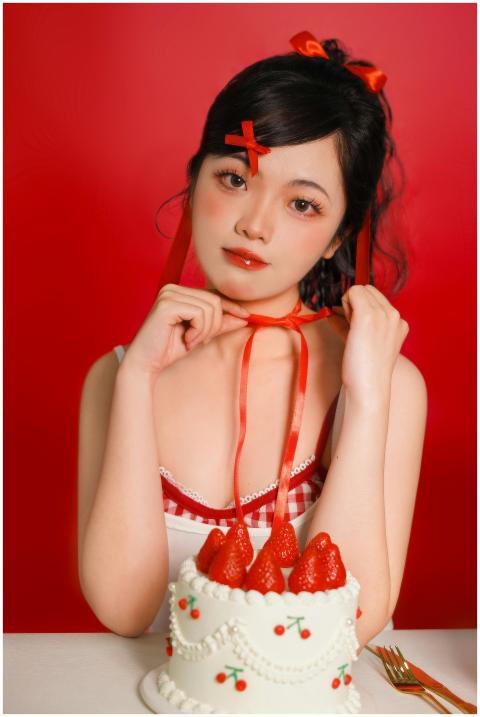 A woman in red ribbon holding a cake with strawber