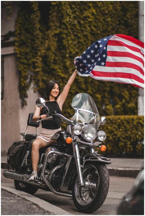 Smiling woman on a motorcycle holding a waving Ame