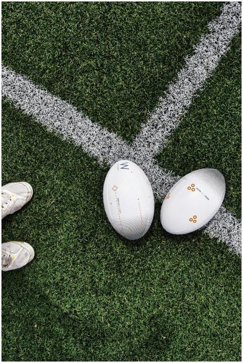 Two rugby balls placed on a grass field with visib