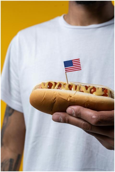 A man in a white t-shirt holding a hot dog with mu