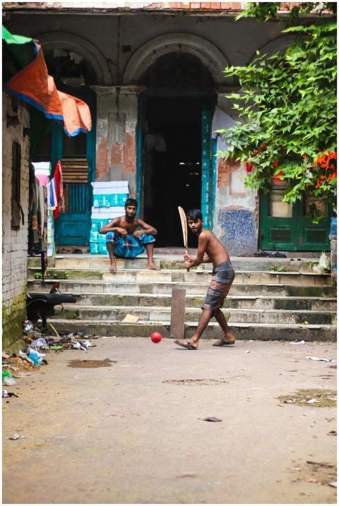 Two young men play street cricket on a vibrant urb