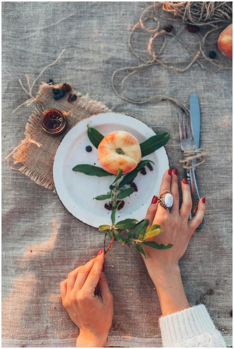 Top view of a rustic dining setup with hands, frui