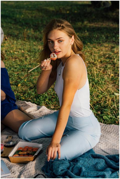 A woman enjoys sushi with chopsticks during a picn