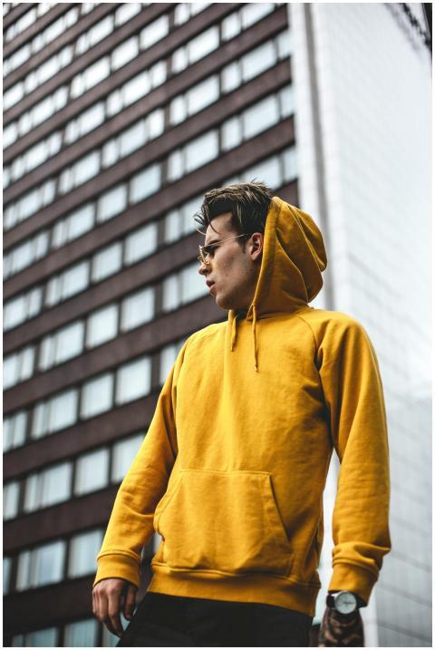 Stylish man poses in yellow hoodie against urban b