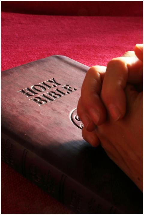 Close-up of hands praying on a Holy Bible, symboli