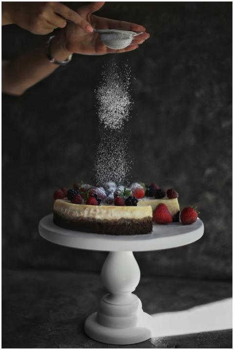 Elegant cheesecake with fresh berries being sprink