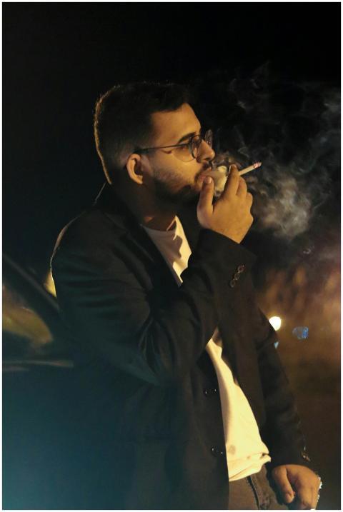 A man with eyeglasses and short hair smokes a ciga