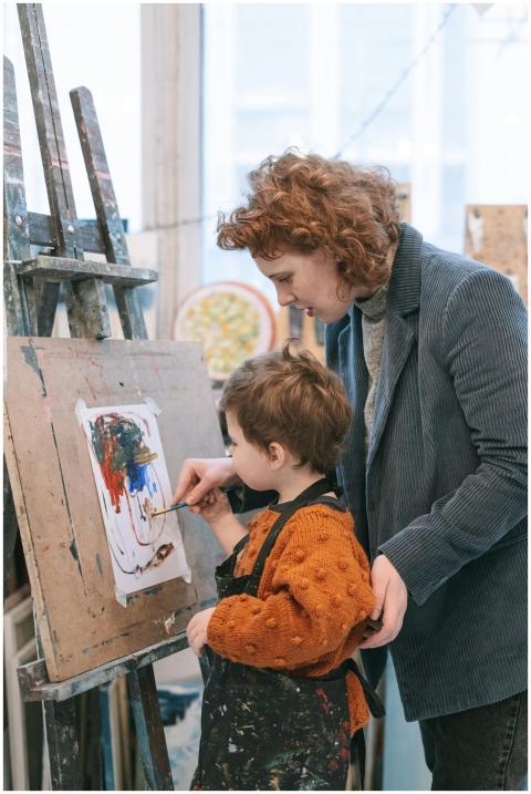 A young child learning to paint with guidance from