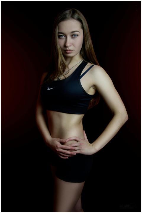 A fit woman poses confidently in a dark studio wea