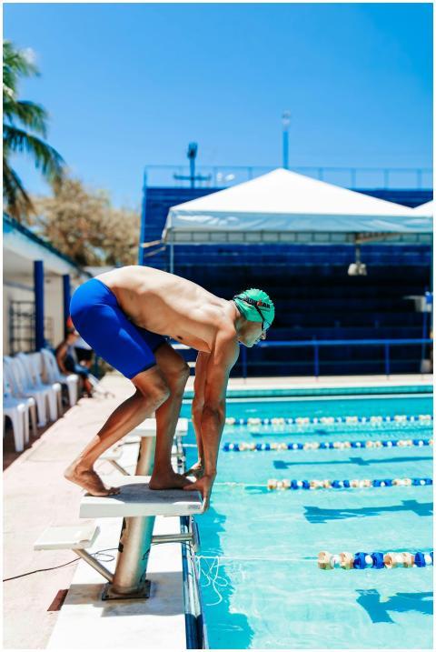 Male swimmer in blue shorts poised to dive at an o