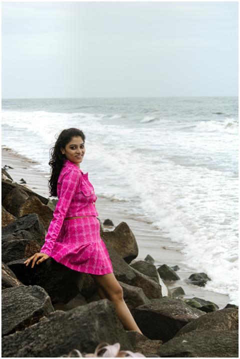 Woman in a pink dress sitting on rocks by the ocea