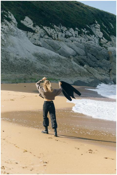A woman stands on a sandy beach by the ocean, embr
