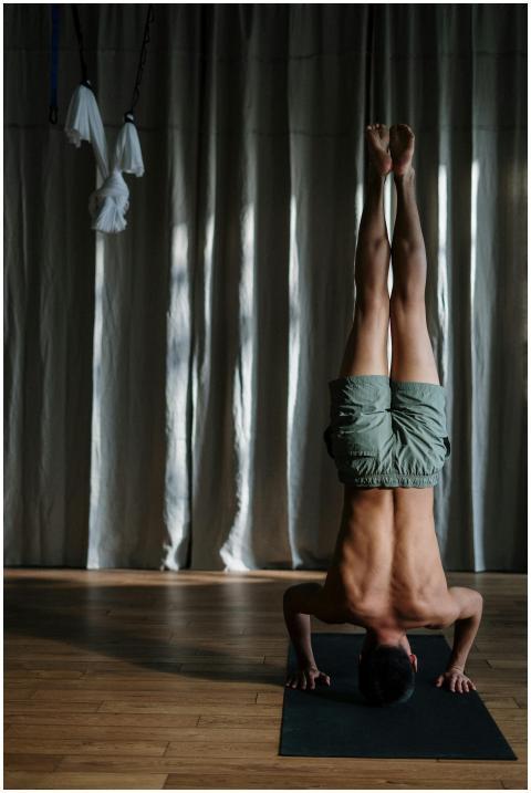 A shirtless man performs a headstand on a yoga mat
