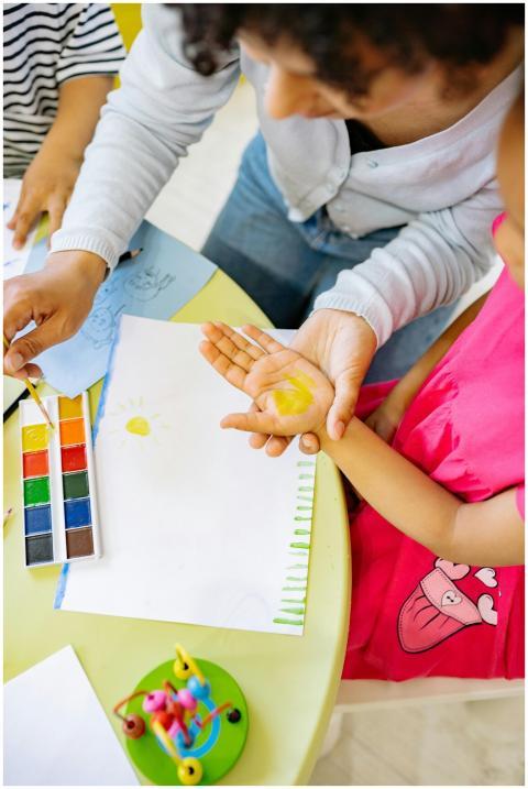A teacher guides a child in art using watercolor p