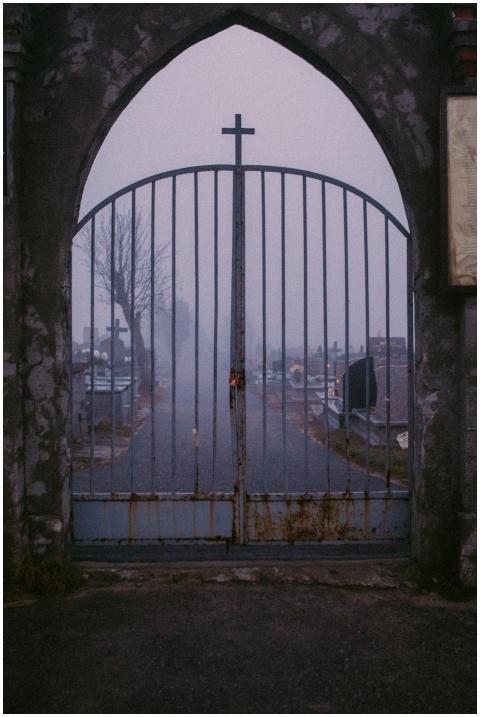 A gloomy cemetery gateway with fog, rusted metal f