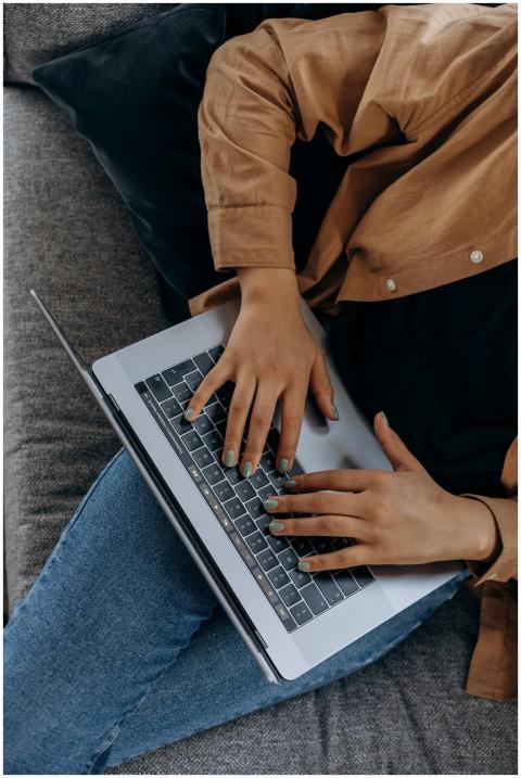 A person typing on a laptop while seated on a couc