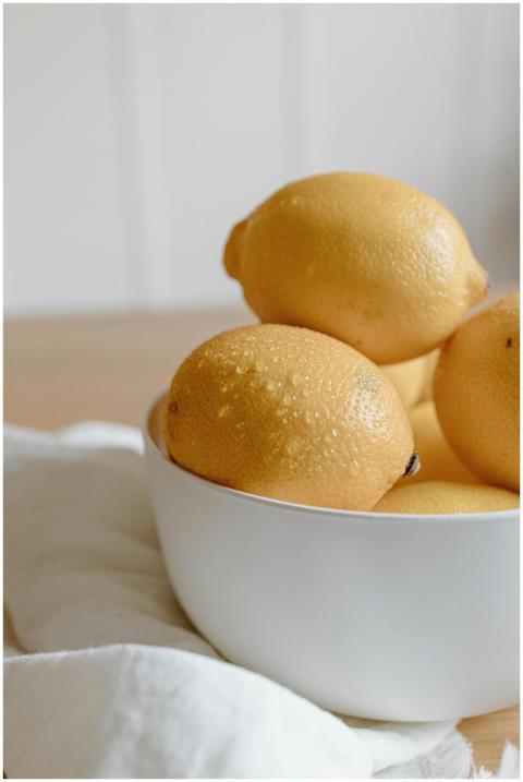 A bowl of fresh lemons on a wooden table with a li