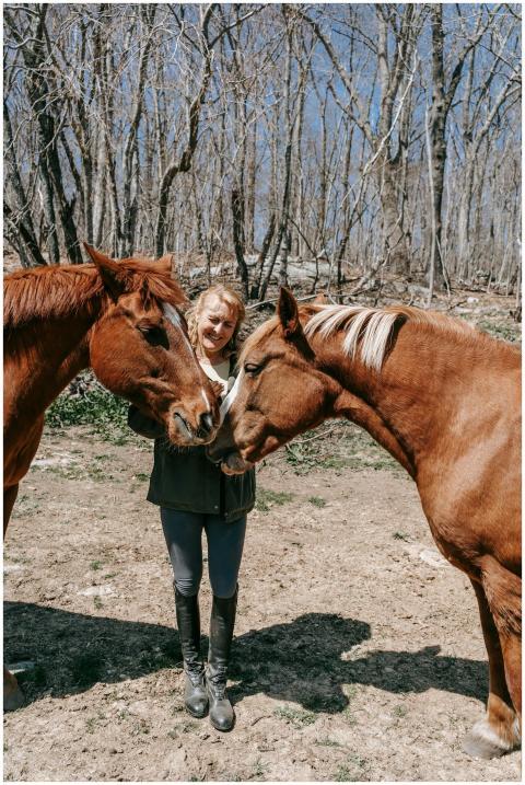 A woman shares a moment with two horses in a sunli
