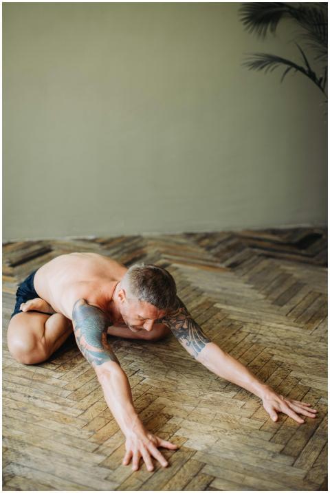A tattooed man engaging in yoga stretches on a woo