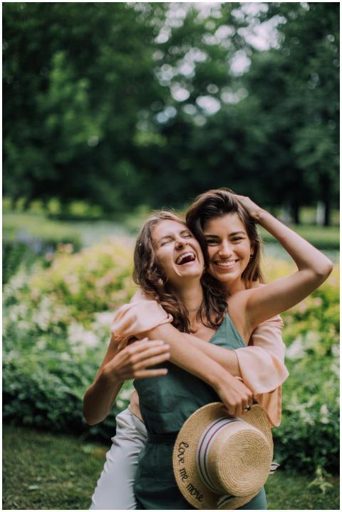 Two women laughing and hugging outdoors in a lush