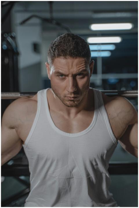 A focused man in a white tank top lifting weights