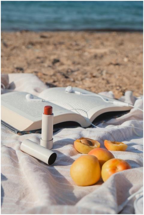 Apricots, book, and lipstick on a beach blanket by