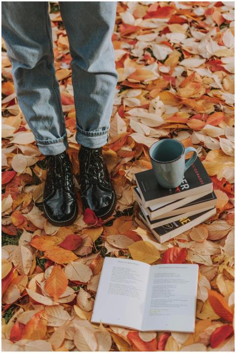 A person stands among autumn leaves with books and