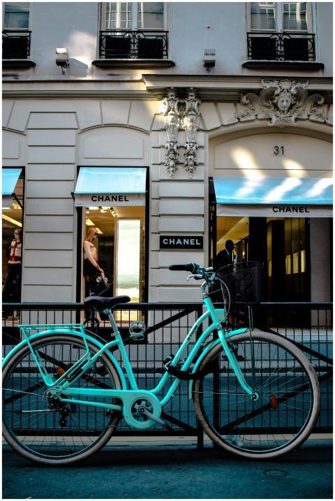 A turquoise bicycle parked in front of a Chanel st