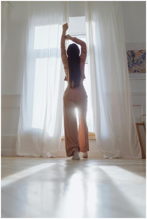 Silhouette of a woman standing in sunlight by a wi