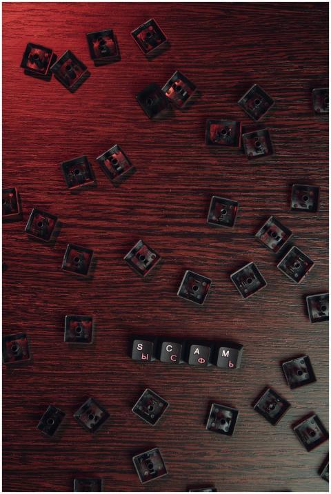 Scattered keyboard keys spelling 'SCAM' on a red-l