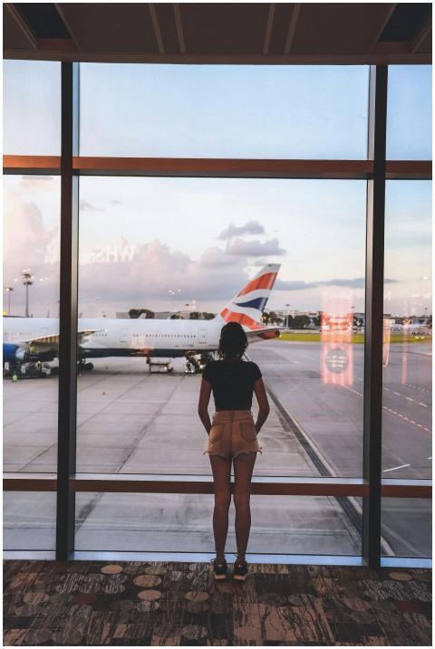 A woman stands at a glass window viewing airplanes