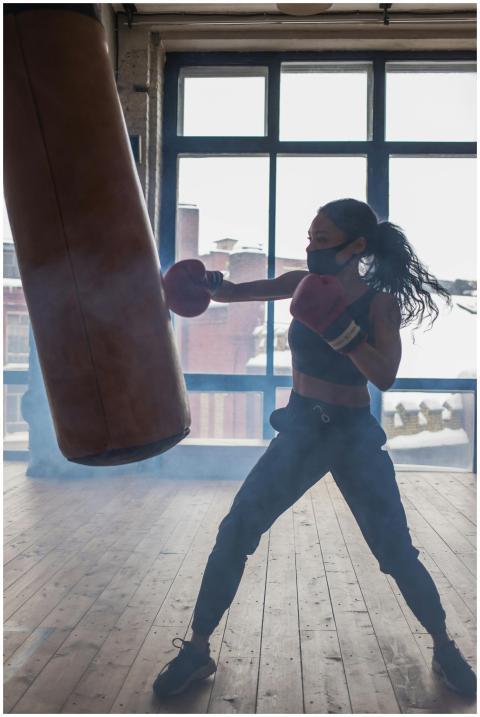 A woman boxer in a mask trains with a punching bag