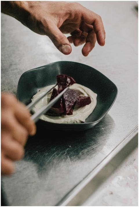 Close-up of a chef's hands garnishing a beetroot d