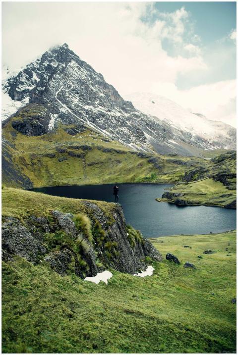 A hiker stands on a cliff overlooking a serene mou