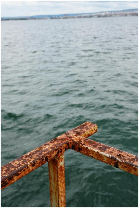 A rusty metal railing with ocean waves and distant